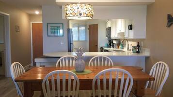A dining area with a wooden table and white chairs, a decorative vase, and a kitchen in the background.