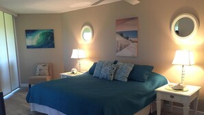 A bedroom with a large bed, two bedside tables with lamps, a round mirror, and artwork on the walls. - Ocean Gate at Hibiscus Resort (St. Augustine)