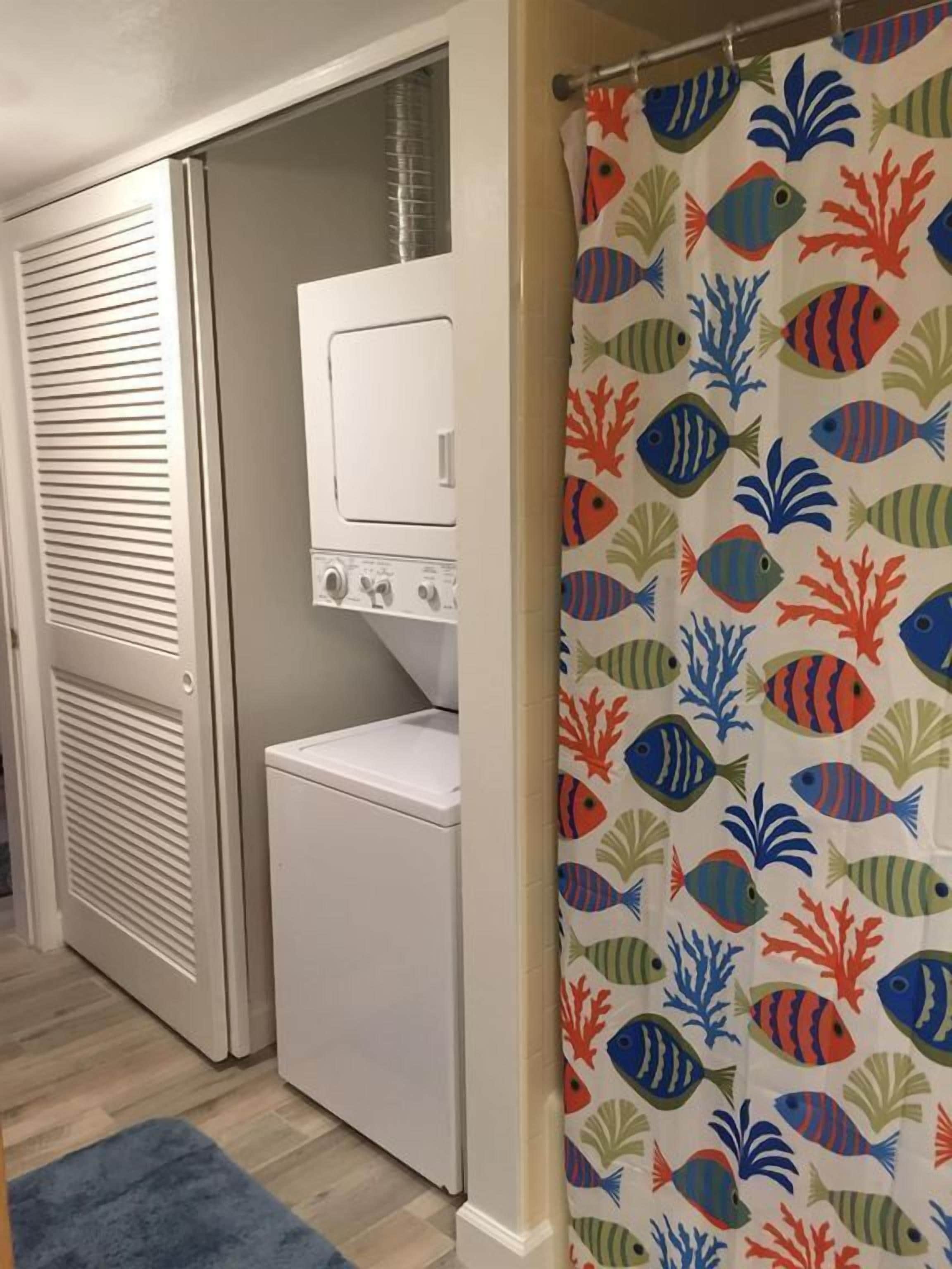 A laundry room with a white washer and dryer, a vented door, and a shower curtain with a fish pattern.