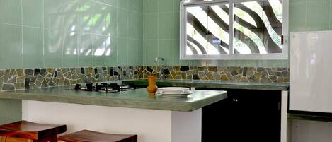 A kitchen with a green tiled backsplash, a window with a view, a stove, and two wooden stools.