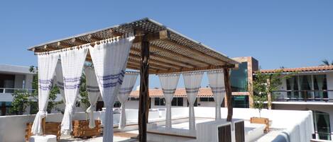 A rooftop terrace with a pergola, white curtains, and outdoor seating.