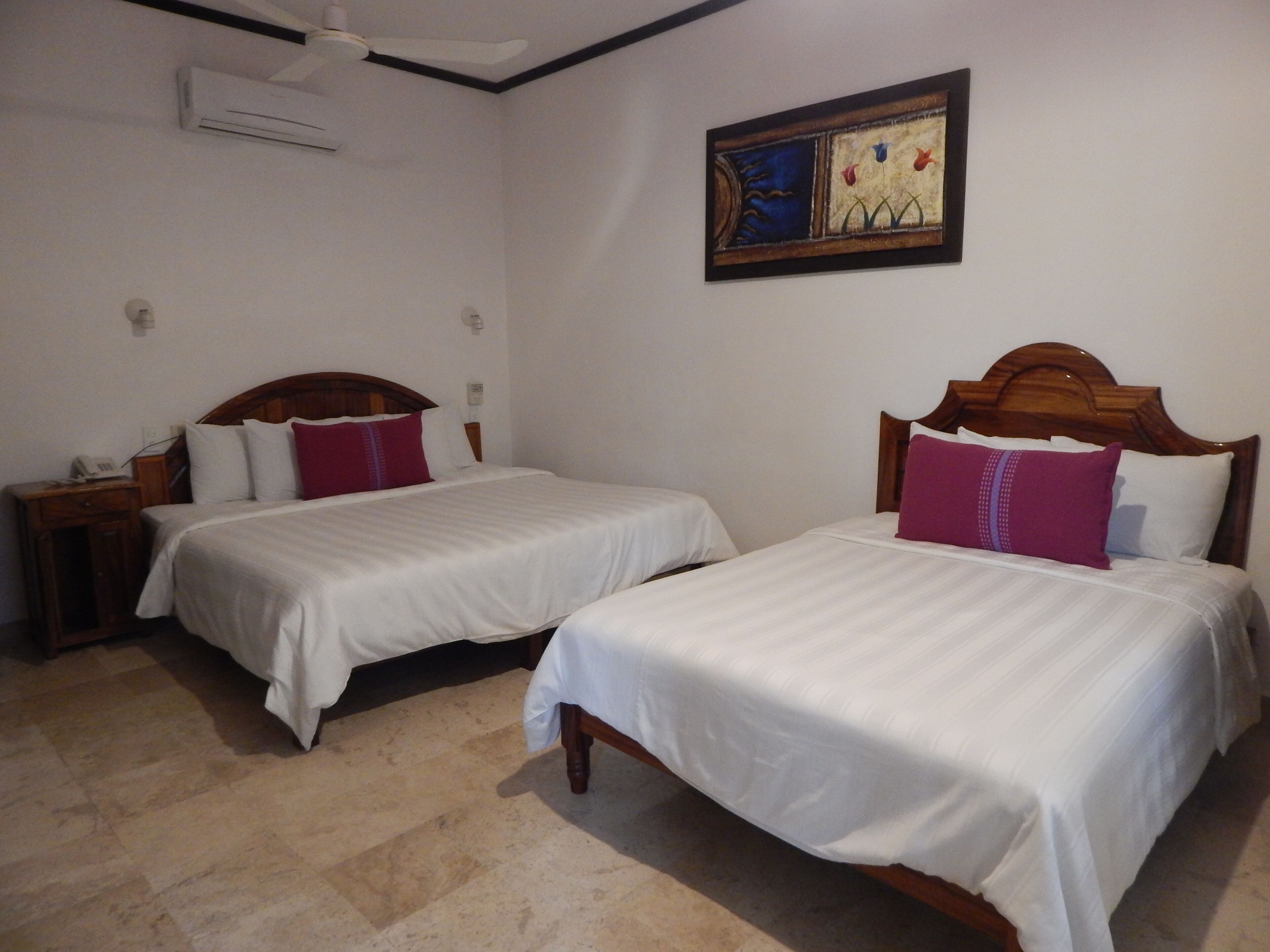 A hotel room with two beds, a wooden headboard, a nightstand with a phone, and a wall-mounted air conditioner.