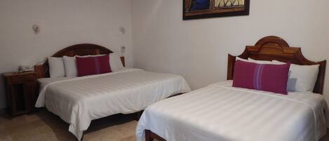 A hotel room with two beds, a wooden headboard, a nightstand with a phone, and a wall-mounted air conditioner.