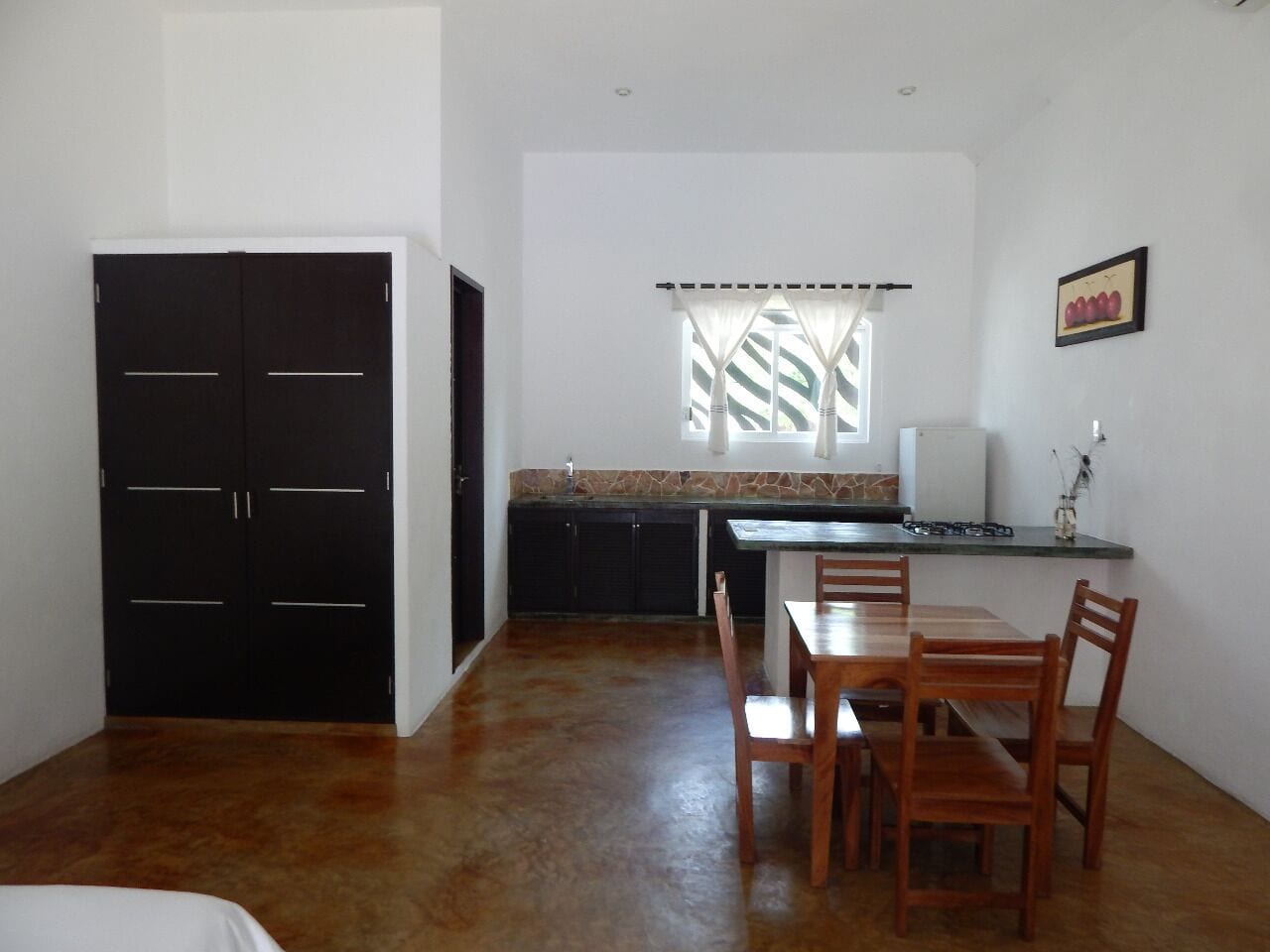 Una cocina compacta con zona de comedor, un armario negro y una ventana con cortinas.