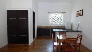 Una cocina compacta con zona de comedor, un armario negro y una ventana con cortinas.