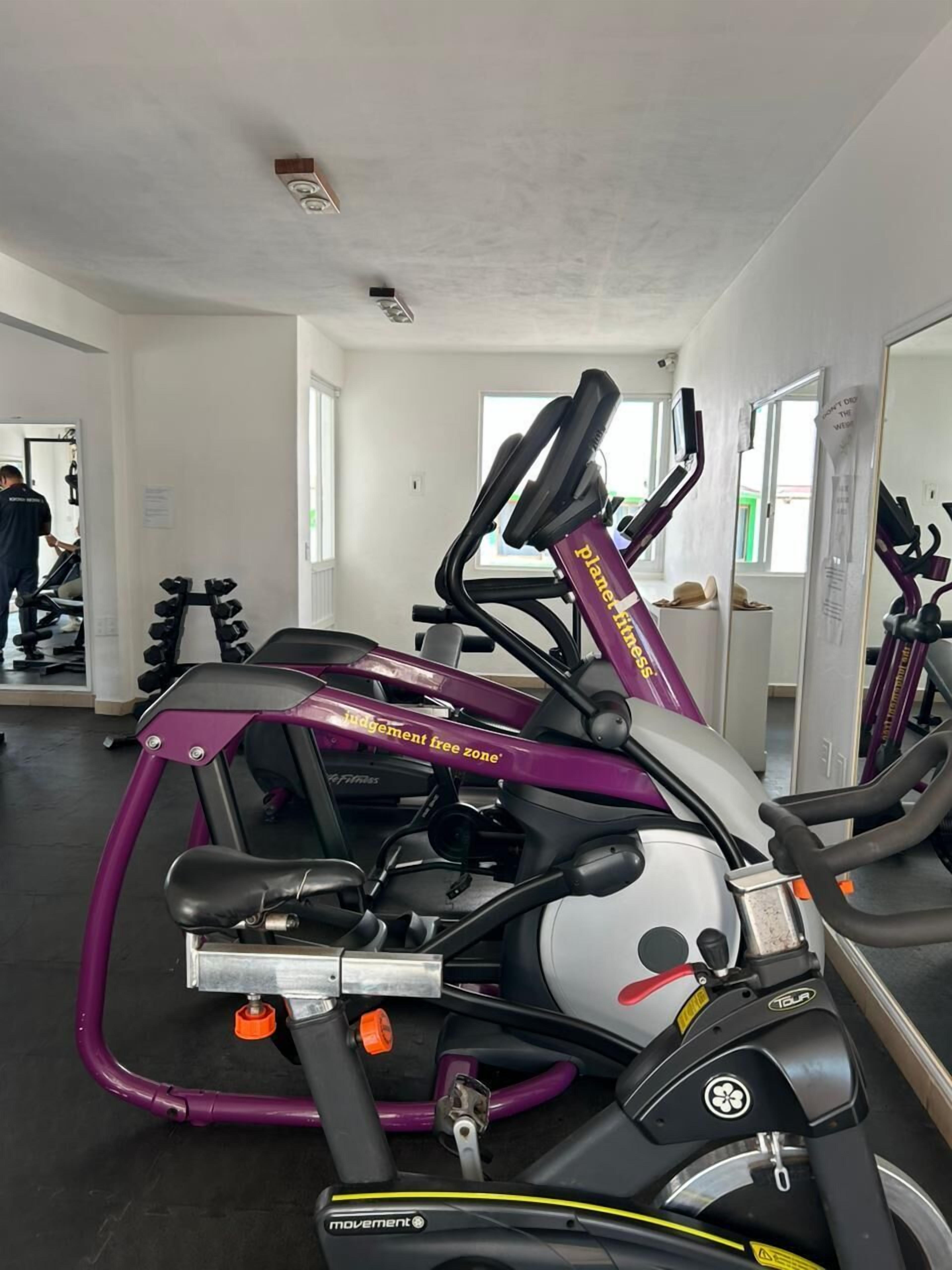 Et fitnessrum med træningsudstyr, herunder en lilla crosstrainer og en motionscykel.