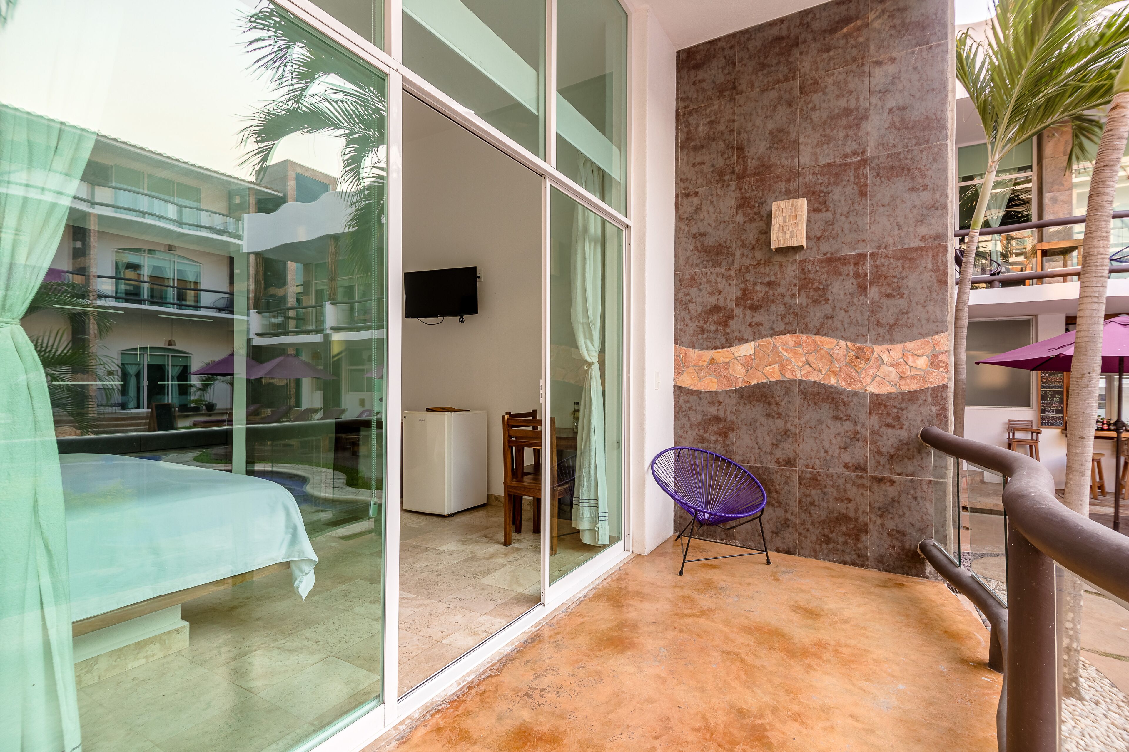 A modern hotel room with a balcony, a large window, and a stone accent wall.