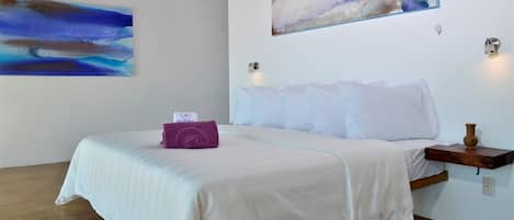 Una habitación de hotel con una cama, un cuadro en la pared y una mesita con un florero.