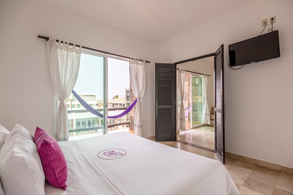 Habitación de hotel con cama, televisión y balcón con vistas.
