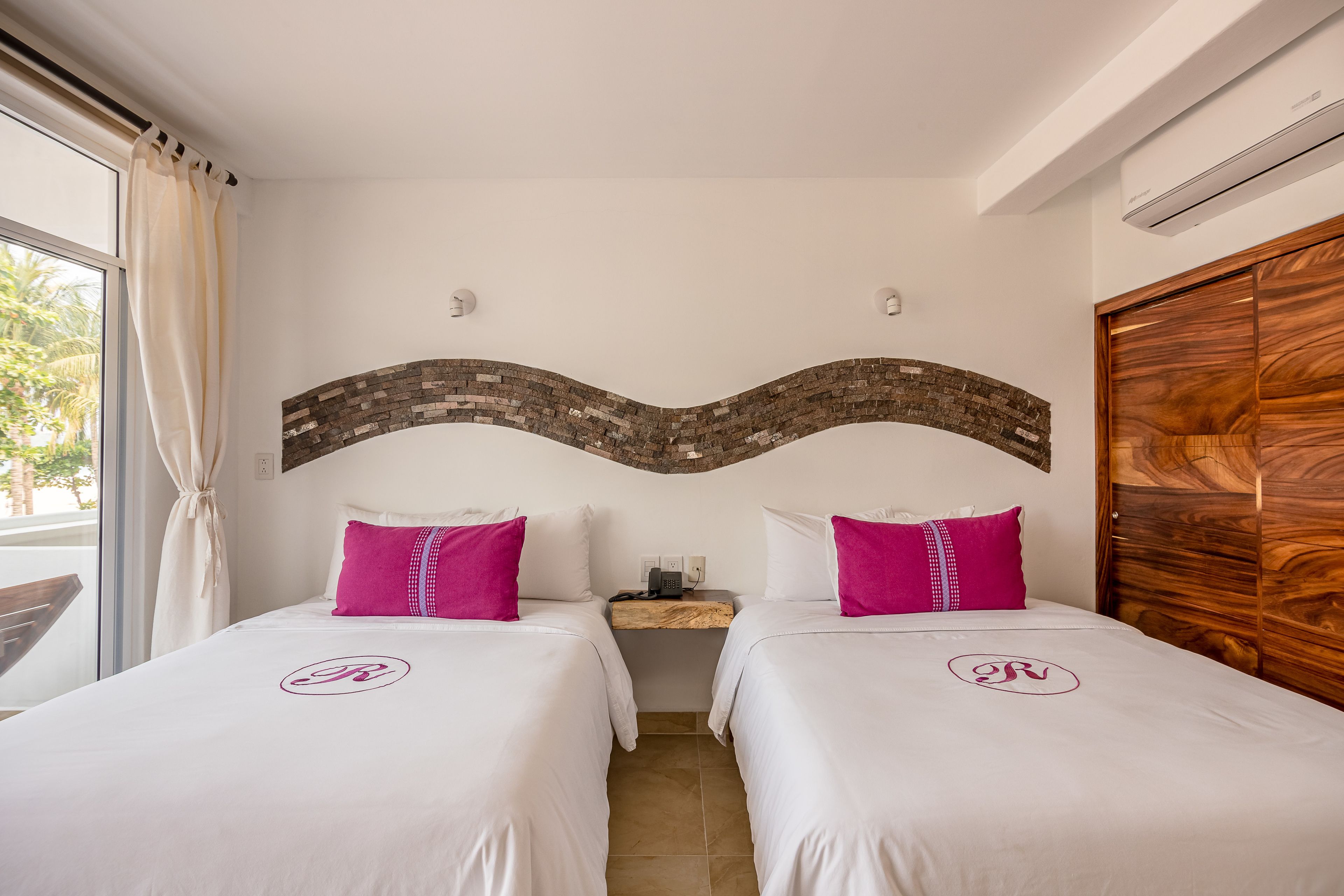A hotel room with two beds, each with a white bedspread and a pink pillow, and a wooden headboard.
