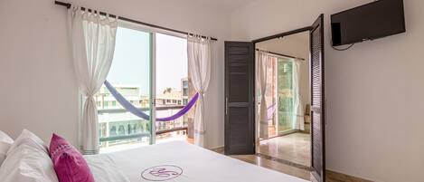 A hotel room with a bed, a TV mounted on the wall, and a balcony with a view of buildings.