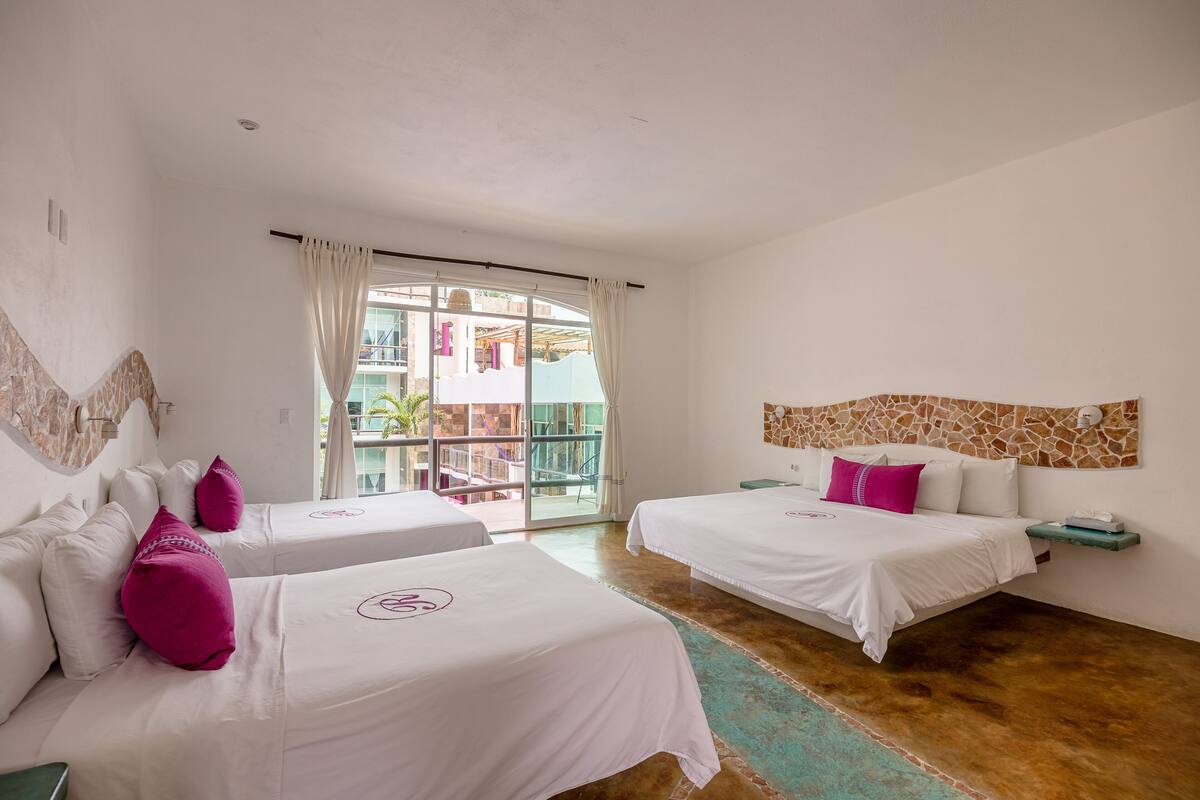 Habitación de hotel con dos camas, un balcón y vistas a un edificio.