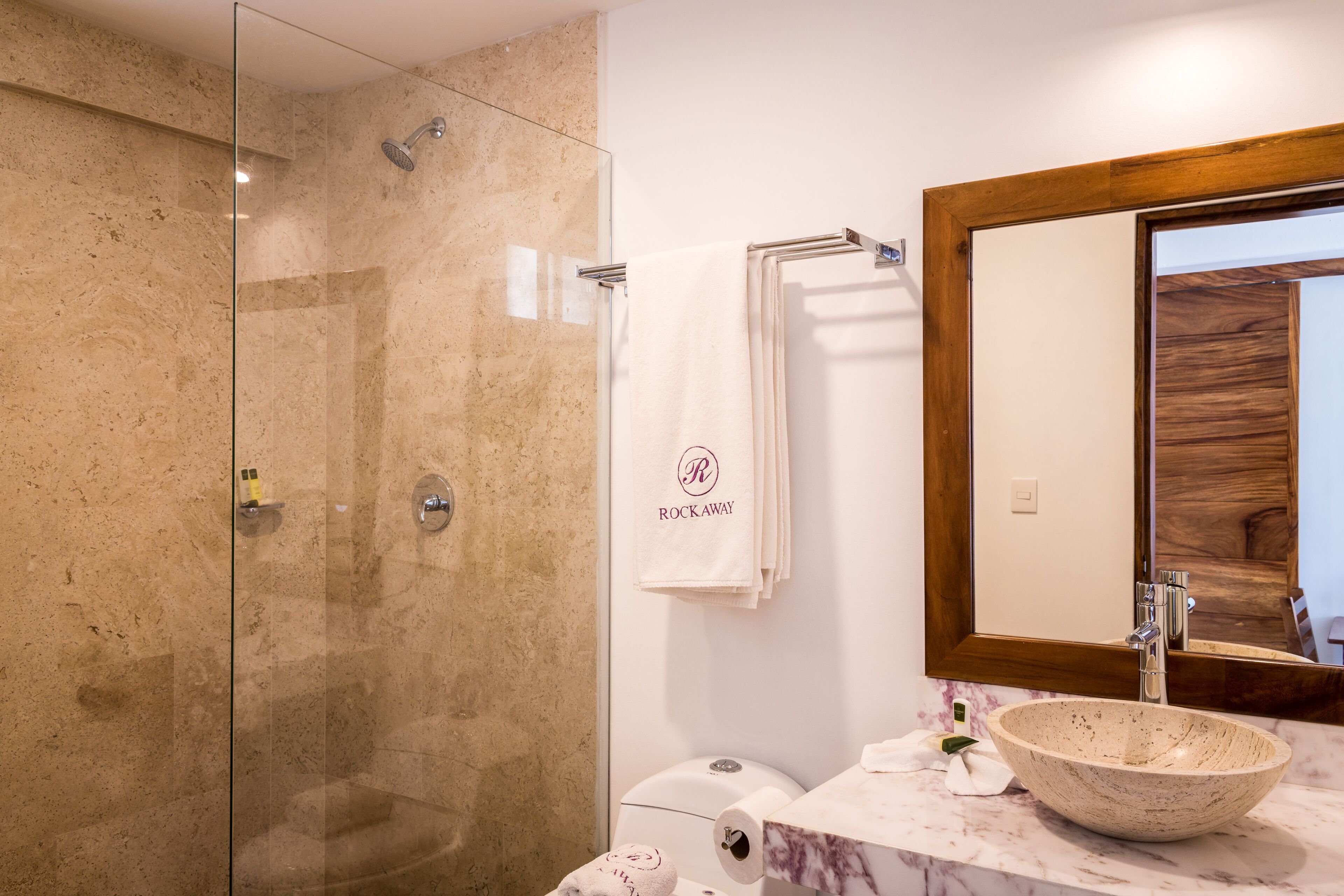 Un baño con ducha envuelta en vidrio, un lavamanos de mármol y un espejo con marco de madera.
