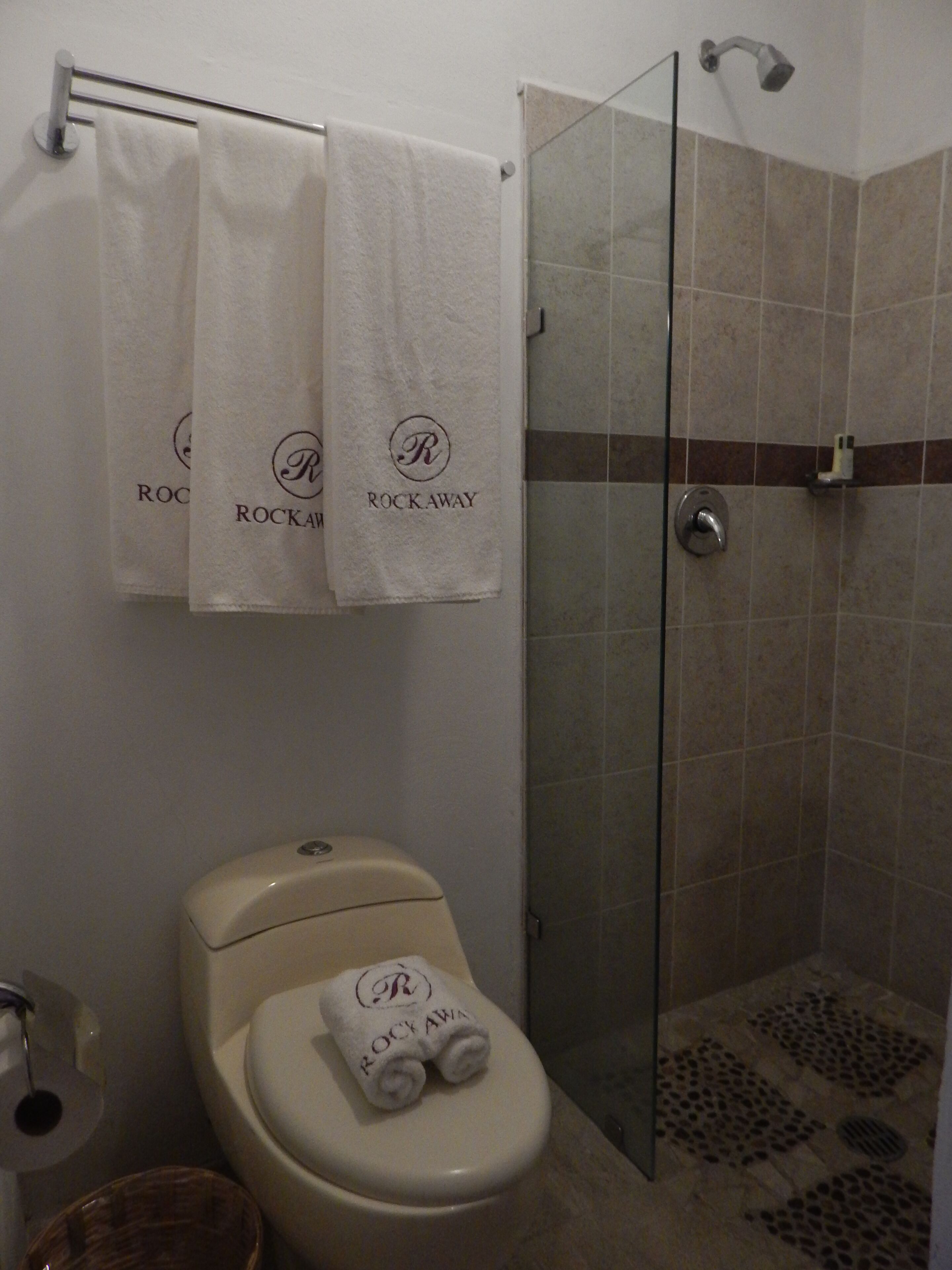 A bathroom with a toilet, a glass shower enclosure, and two towels hanging on a rack with the logo "Rockaway".