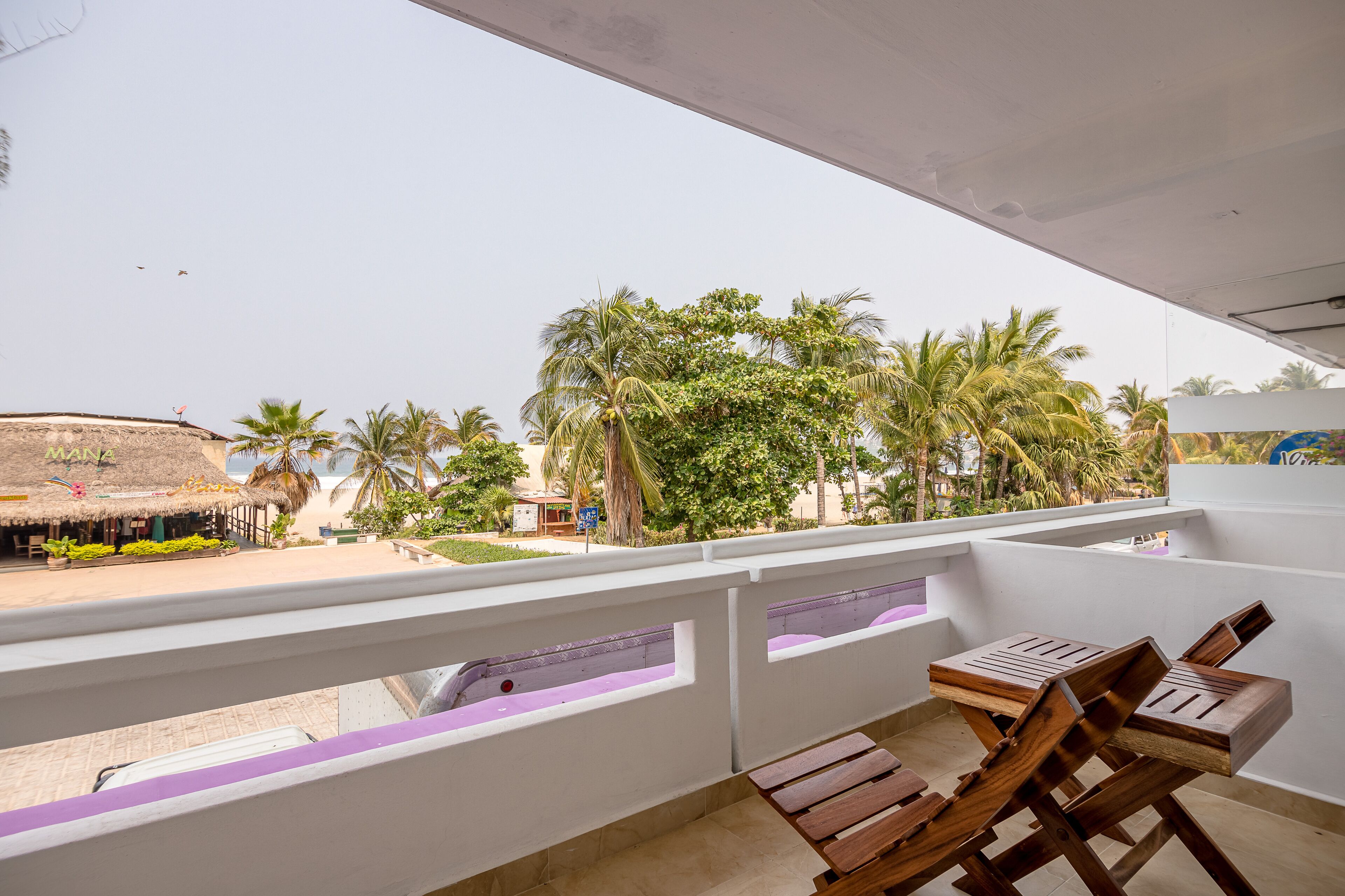 Un balcone con mobili in legno, vista su una spiaggia e palme.