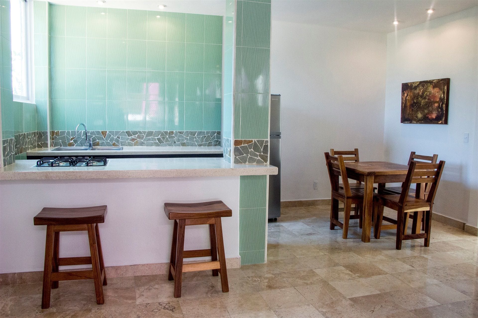 Una cocina con salpicadero de azulejos, estufa a gas, lavamanos y comedor con sillas y mesa de madera.
