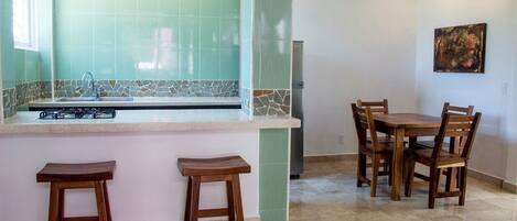 Una cocina con salpicadero de azulejos, estufa a gas, lavamanos y comedor con sillas y mesa de madera.