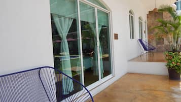 A covered patio area with a large sliding glass door, a potted plant, and two blue chairs.
