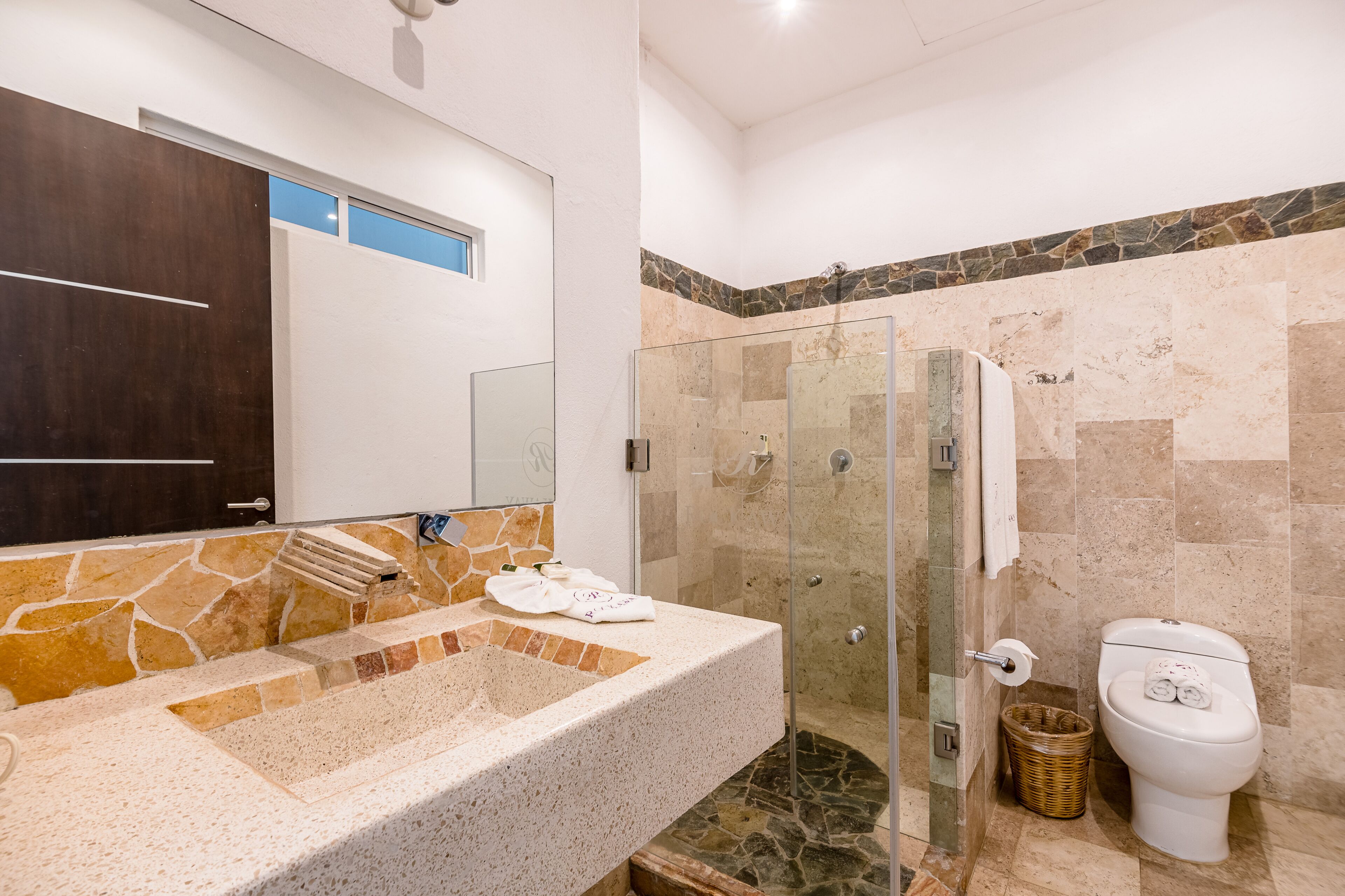 Un baño con lavamanos de piedra, cabina de ducha con mampara de vidrio y un inodoro.