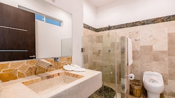 Un baño con lavamanos de piedra, cabina de ducha con mampara de vidrio y un inodoro.