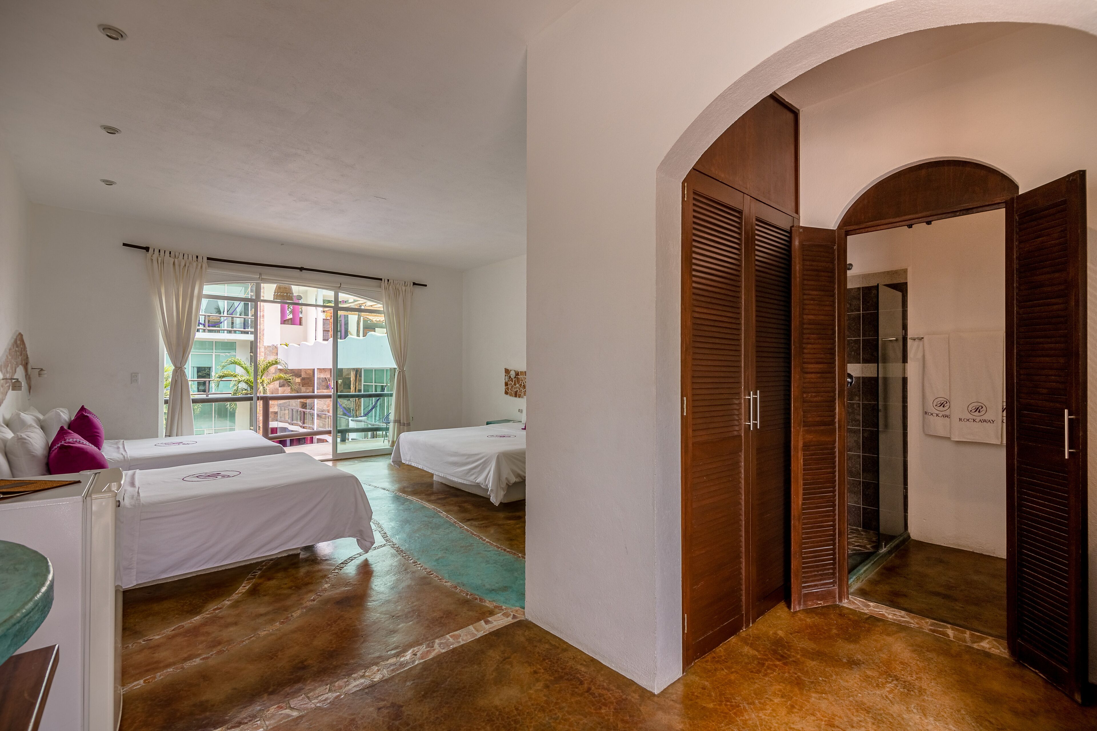 A hotel room with two beds, a large window, and a wooden wardrobe.