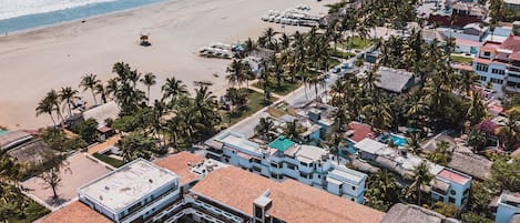 Vista aérea de un complejo turístico costero con varias edificaciones, una playa y una vista despejada del océano.