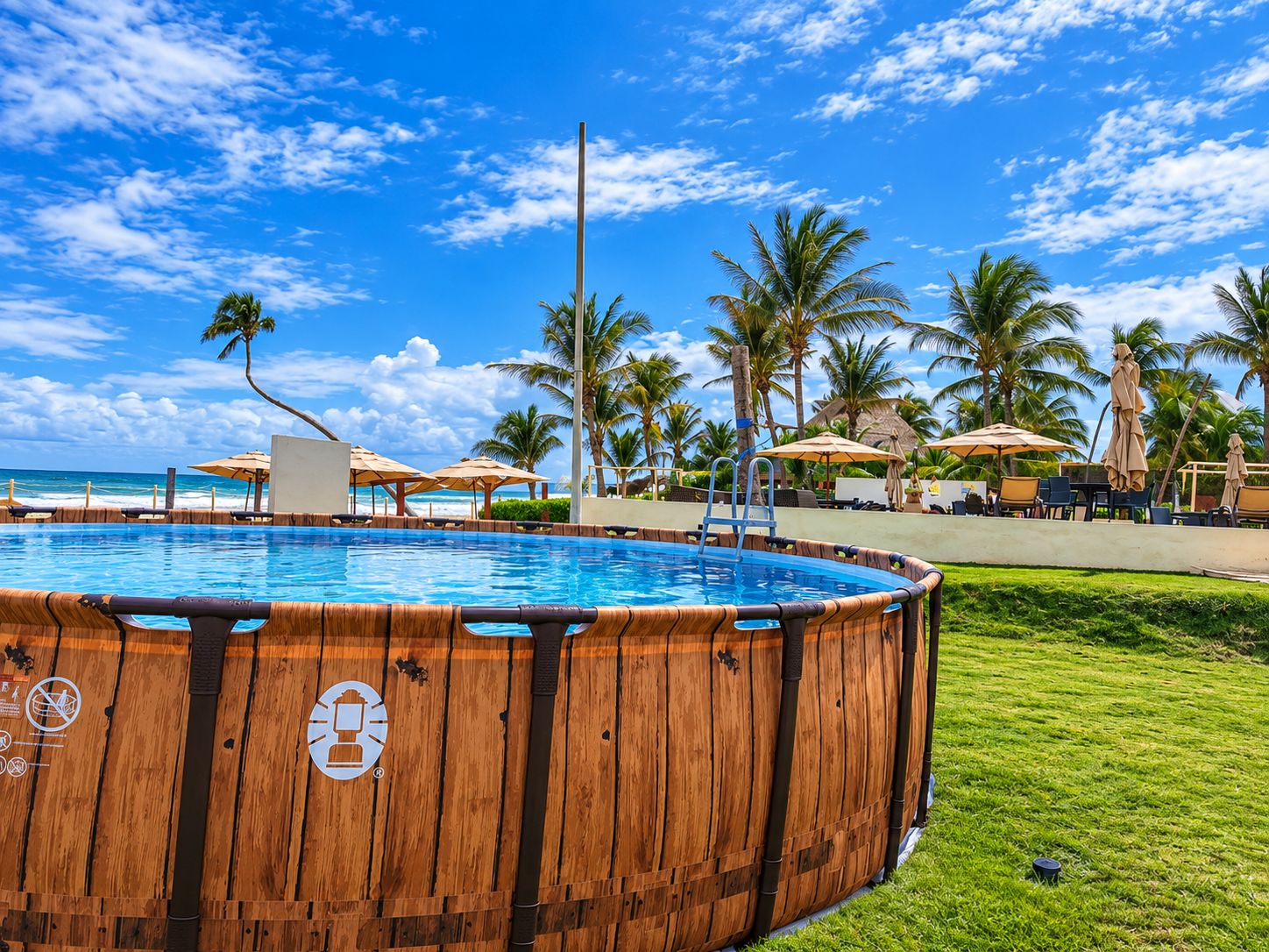 Un jacuzzi de madera rodeado por una piscina, palmeras y sombrillas de playa.