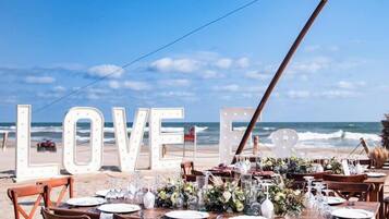 An outdoor dining setup with tables and chairs, large illuminated letters spelling "LOVE FOR," and a view of the ocean.