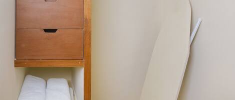 Una habitación pequeña y funcional con un armario de madera, un estante con toallas dobladas, un microondas y una percha para ropa.