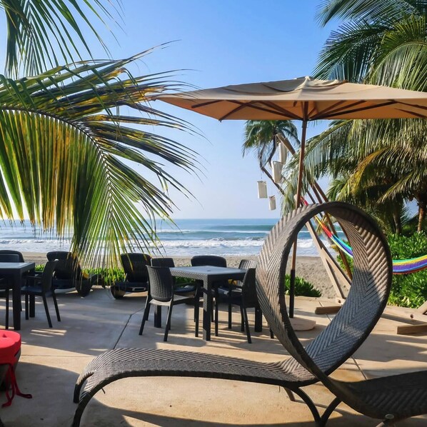 An outdoor seating area with tables and chairs, a large umbrella, and a view of the ocean. - Mishol Bodas Hotel & Beach Club Acapulco Diamante (Acapulco)