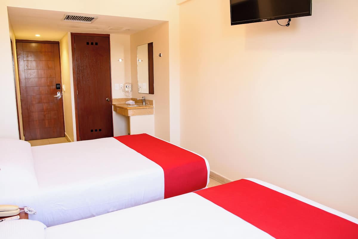 Een hotelkamer met twee bedden, een badkamer met een wastafel en spiegel, en een aan de muur bevestigde televisie.