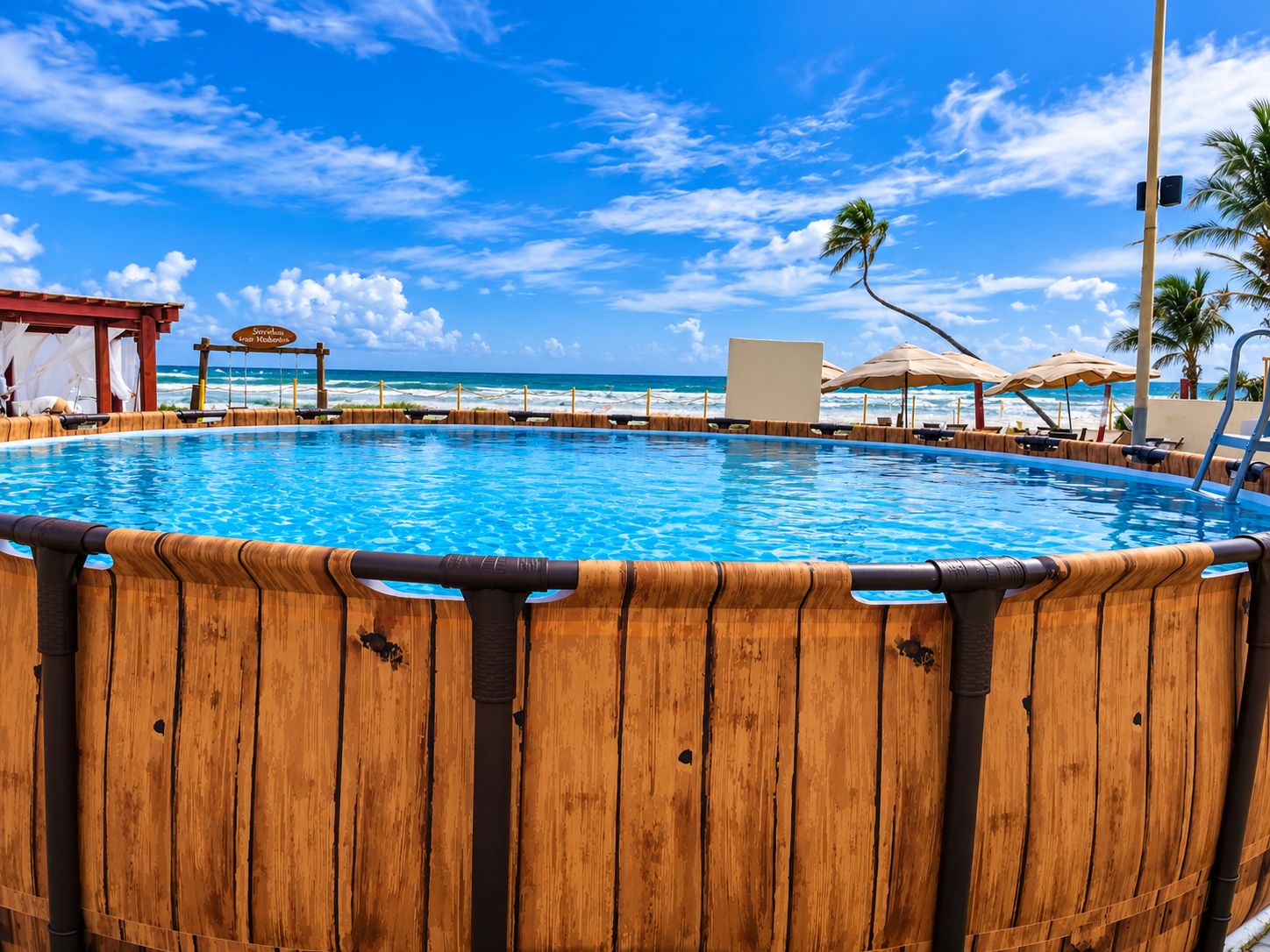 Une piscine en bois entourée de parasols de plage et de chaises longues, avec vue sur l’océan et un ciel dégagé.