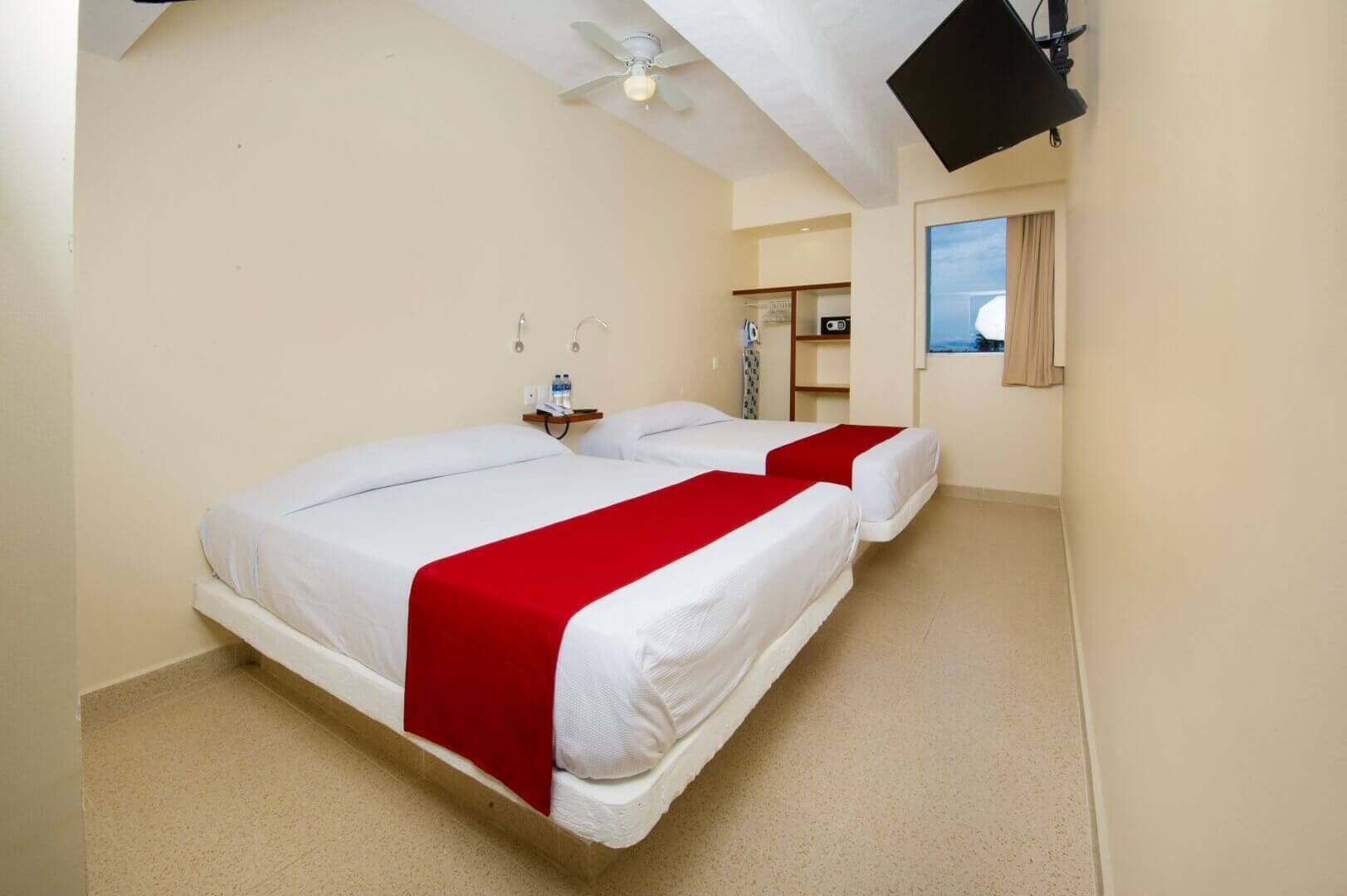 A hotel room with two beds, a ceiling fan, a flat-screen TV, and a window with curtains.