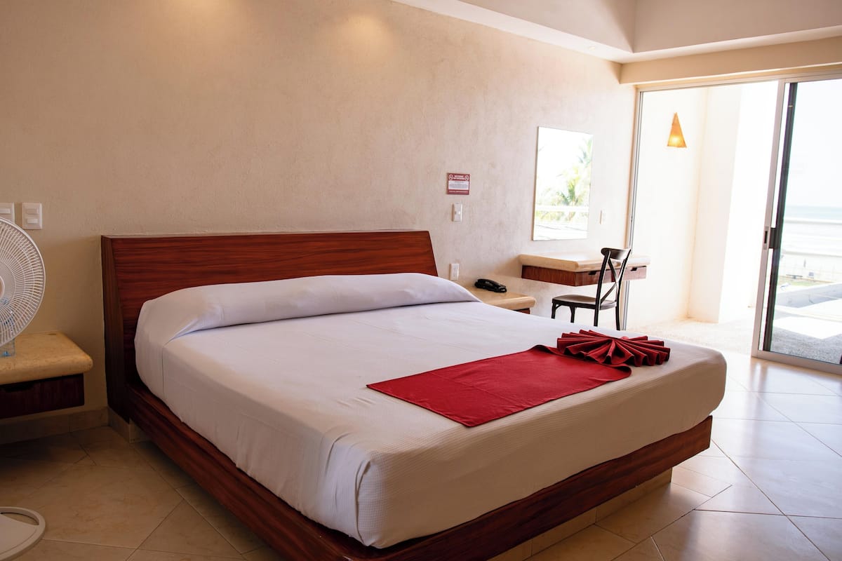 Een hotelkamer met een groot bed, een nachtkastje, een stoel, een bureau en uitzicht op de omgeving.
