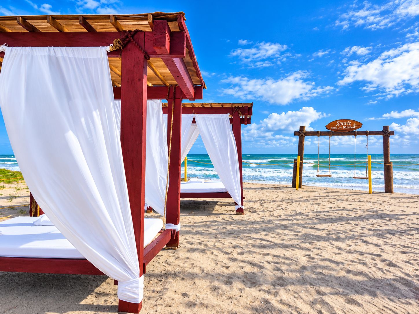 Una playa con una estructura de cama de madera, cortinas blancas y un columpio.