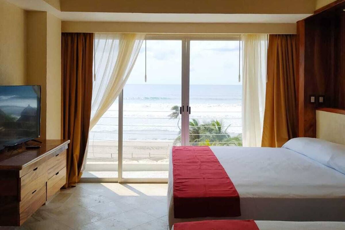Een hotelkamer met twee bedden, een plafondventilator, een televisie en uitzicht op de oceaan.