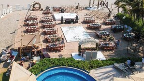 Montaje para una boda en la playa, con mesas y sillas dispuestas para los invitados, un escenario y una piscina.
