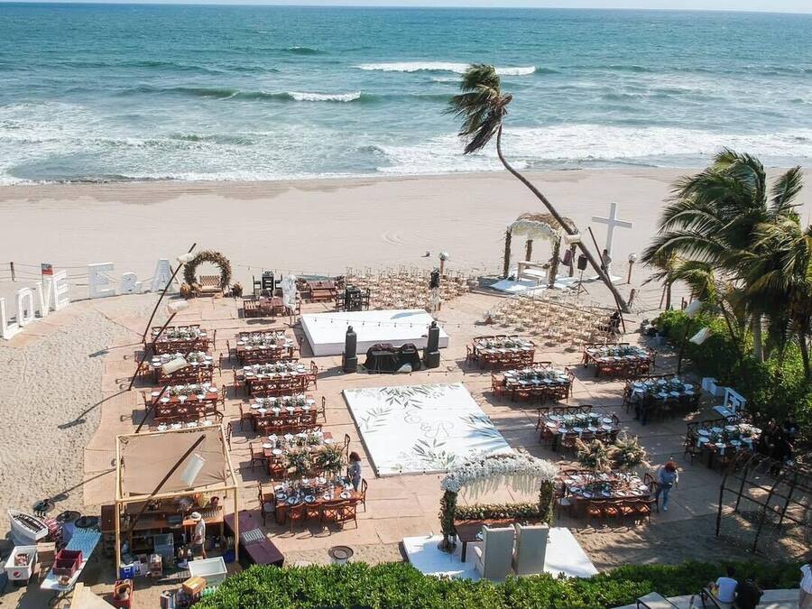 A beachside wedding setup with tables and chairs arranged for guests, a stage, and a pool.