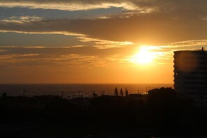 Een zonsondergang boven een kuststadsgezicht, met een opvallend gebouw op de voorgrond.