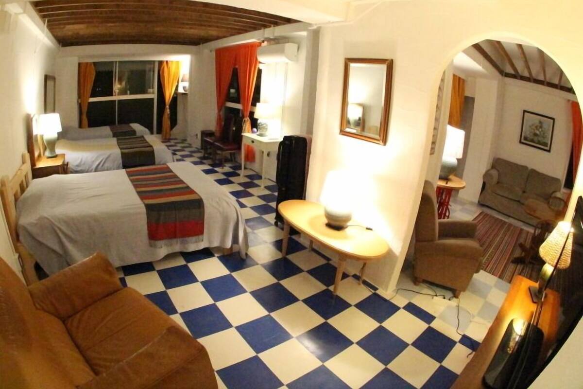 Una habitació d'hotel amb dos llits, un sòl a quadres, una taula petita amb una làmpada, un sofà i un mirall a la paret.