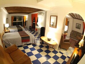 Een hotelkamer met twee bedden, een zwart-wit schaakbordvloer, een klein tafeltje met een lamp, een bank en een spiegel aan de muur.