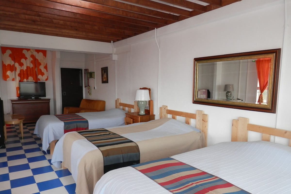 Habitació d'hotel amb tres llits individuals, televisió, escriptori i mirall.