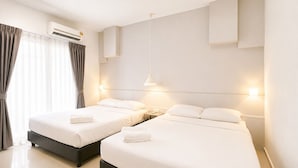 Habitación de hotel con dos camas, aire acondicionado, una mesita de noche con lámpara y una ventana con cortinas.