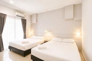 A hotel room with two beds, an air conditioning unit, a bedside table with a lamp, and a window with curtains. - Grand Swiss Hotel (George Town)
