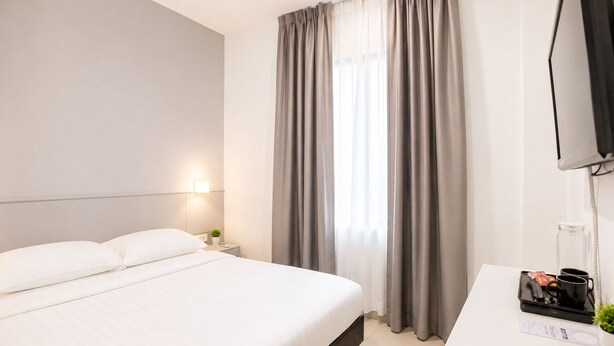 Una habitación de hotel con cama, escritorio, televisor y ventana con cortinas.
