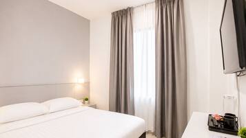 Una habitación de hotel con cama, escritorio, televisor y ventana con cortinas.