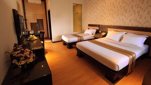 Ein Hotelzimmer mit zwei Betten, einem Schreibtisch mit Blumenvase, einem Spiegel und einem Kleiderschrank.