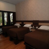 Habitación de hotel con tres camas individuales, suelo de madera, un ventanal grande y pared con diseño.