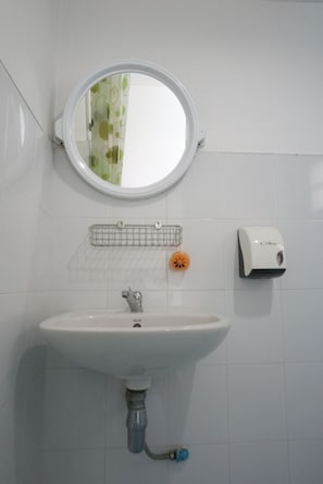 A bathroom with a white sink, a round mirror, a soap dispenser, and a small orange soap dish.