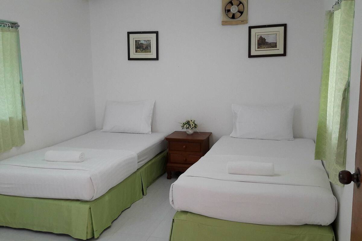 A room with two single beds, a nightstand with a vase of flowers, and two framed pictures on the wall.
